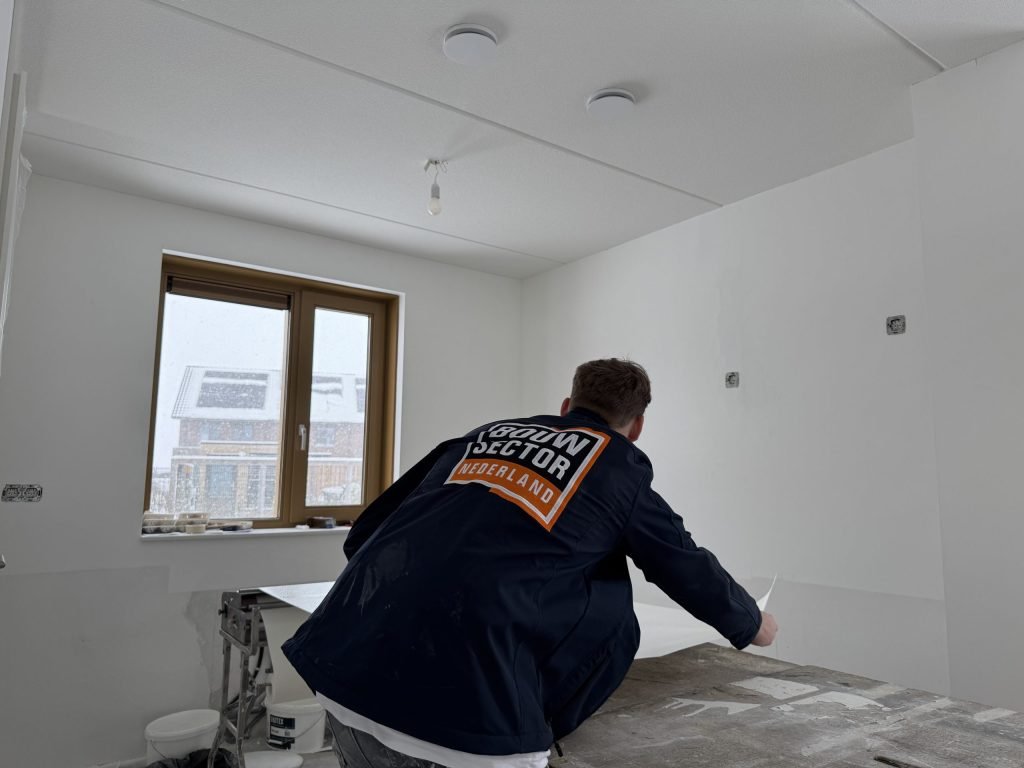 Vakman van Bouwsector Nederland legt een baan behang klaar op de plaktafel