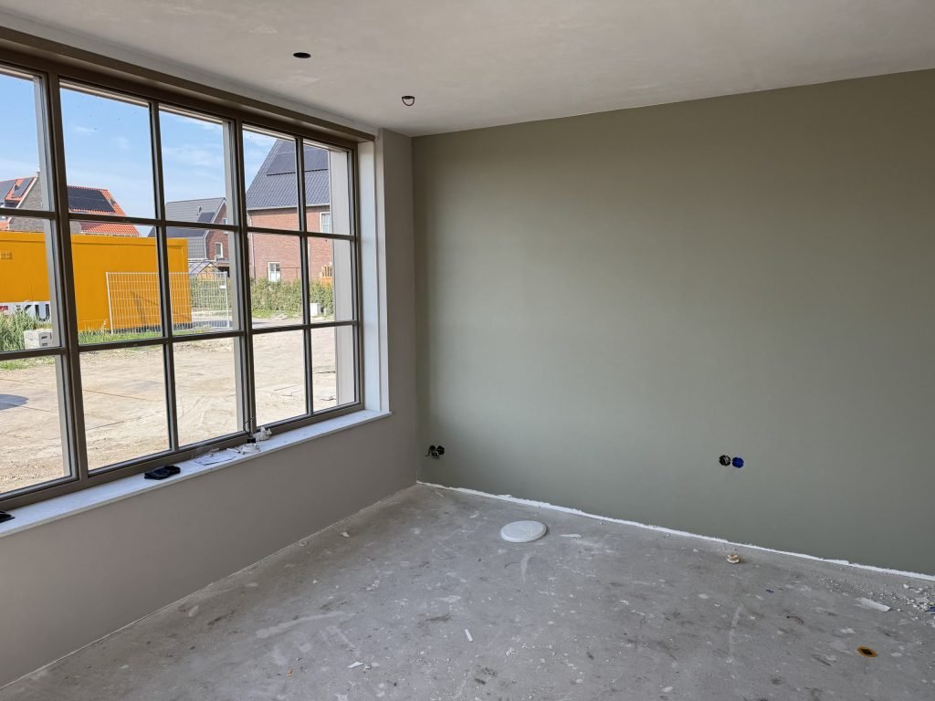 Kamer met een egaal gesausde wand in een grijsgroene tint naast een groot raam